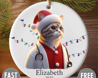 Könnte beinhalten: Runder Weihnachtsschmuck mit einer Katze als Arzt, die einen Weihnachtsmannhut und ein Stethoskop trägt. Der Schmuck trägt den Namen "Elizabeth" und das Jahr "-2025-". Bunte Lichterketten sind um die Katze herum gezeichnet.