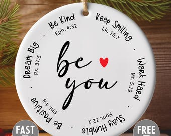 May include: Round white ceramic ornament with the words "be you" in black script, a red heart, and inspirational phrases. Includes the text "Dream Big," "Be Kind," "Keep Smiling," "Work Hard," "Be Positive," and "Stay Humble."