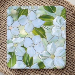 Puede incluir: Posavasos cuadrado con un diseño de vidriera con flores blancas y hojas verdes. El patrón floral se establece sobre un fondo azul claro y verde, creando un aspecto decorativo y artístico.