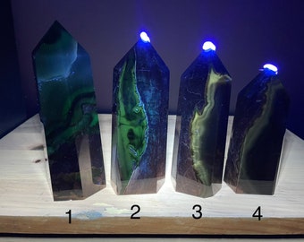 Könnte beinhalten: Vier grüne und schwarze Kristalltürme mit einer spitzen Spitze, nummeriert von 1 bis 4. Die Türme werden von oben mit einem blauen Licht beleuchtet.