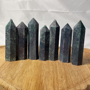 Puede incluir: Siete obeliscos de cristal verde oscuro y burdeos de diferentes alturas están dispuestos sobre una bandeja de madera. Los obeliscos tienen un diseño facetado y puntas puntiagudas. La bandeja tiene un borde festoneado y veta de madera natural.