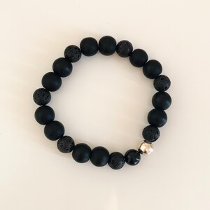 May include: Black beaded bracelet with a silver bead accent. The bracelet is made with black lava rock and matte black beads.