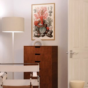 Peut inclure: Une lampe blanche avec un abat-jour en tissu blanc se trouve &agrave; c&ocirc;t&eacute; d'un fauteuil blanc avec une structure en bois. Une commode &agrave; quatre tiroirs se trouve derri&egrave;re le fauteuil. Une estampe encadr&eacute;e de corail et d'autres formes de vie marine est accroch&eacute;e au mur. La porte est ouverte sur une pi&egrave;ce avec des rideaux blancs.