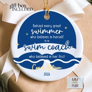 May include: A white ceramic ornament with a blue circular design featuring text that reads, "Behind every great swimmer who believes in herself is a swim coach." Gold text says "Coach Allison" and "2026". A gift box is included.