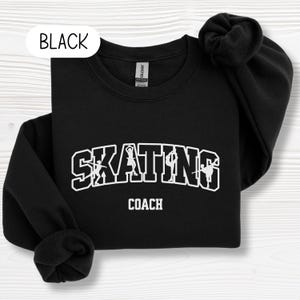 May include: Black sweatshirt with the text "SKATING COACH" in white block letters. The word "SKATING" has silhouettes of skaters within the letters. The word "BLACK" is in a white oval in the upper left corner.