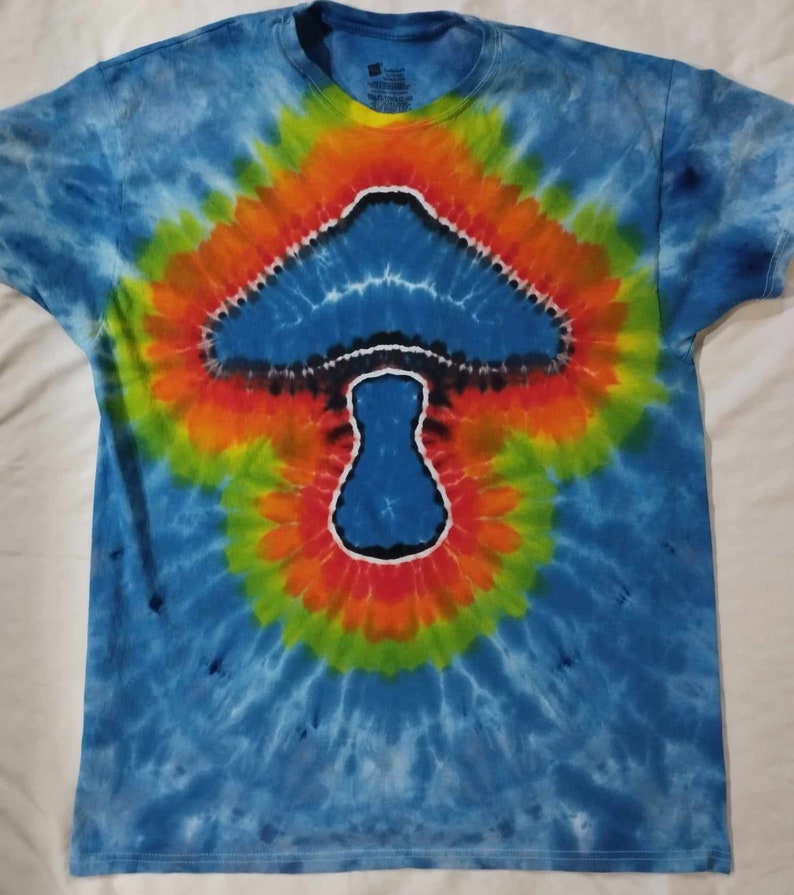 May include: A blue tie-dye t-shirt with a mushroom design in the center. The mushroom is outlined in black and white, and the background is a swirl of blue, green, yellow, and orange.