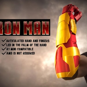 May include: A red and gold Iron Man arm prop, with articulated fingers and LED in the palm. The image includes the text "IRON MAN" and bullet points: "ARTICULATED HAND AND FINGERS", "LED IN THE PALM OF THE HAND", "A1 MINI COMPATIBLE", and "AMS IS NOT REQUIRED".
