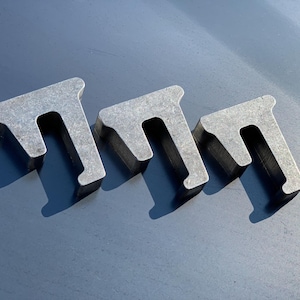 Könnte beinhalten: Drei Metallscheiben in verschiedenen Größen, jede mit einer U-förmigen Öffnung. Die Scheiben sind aus silberfarbenem Metall gefertigt und haben eine raue, unfertige Textur.