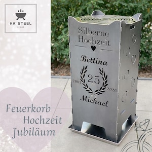 Könnte beinhalten: Ein silberner Metall-Feuerkorb mit ausgeschnittenen Herzformen und Text. Der Text enthält "Silberne Hochzeit", Namen und die Zahlen "25", "2001" und "2026". Der Feuerkorb hat eine quadratische Form und eine Tablettbasis.