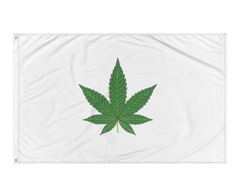 May include: A white flag featuring a large, detailed green cannabis leaf in the center. The leaf has multiple points and veins, set against a plain white background. The flag has grommets for hanging.