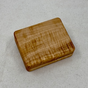 May include: A small, rectangular wooden box with a light brown finish. The wood grain is visible and has a natural, rustic look.