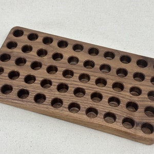 May include: A rectangular wooden tray with 48 round cutouts. The tray is made of dark brown wood and has a natural wood grain.