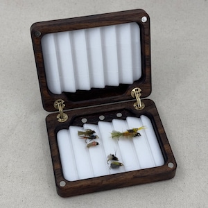 May include: A dark brown wooden fly fishing box with a white foam interior and five compartments. The box is open and contains five flies.