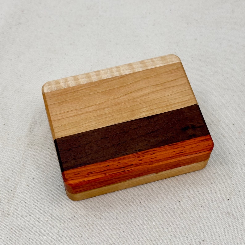May include: A small wooden box with a light wood top, a dark wood middle section, and a reddish-brown bottom.