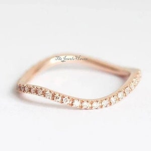 Pode incluir: Um delicado anel de banda de ouro rosa com um design ondulado e uma fileira de pequenos diamantes transparentes.