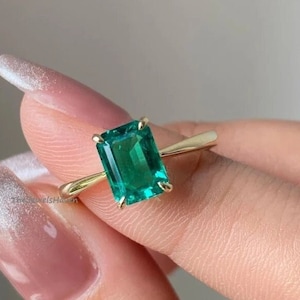 May include: A gold ring featuring a large emerald green gemstone. The gemstone is a rectangular emerald cut.