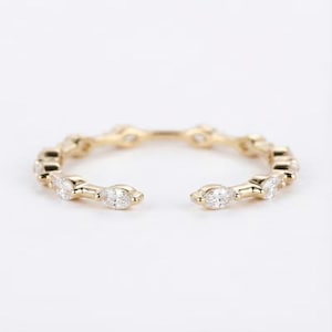 May include: A gold-coloured open ring featuring clear, marquise-cut gemstones. The ring has a delicate, open band design, with the gemstones set along the top half of the ring.