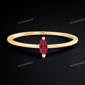 May include: A delicate gold band ring with a single marquise-shaped ruby gemstone.