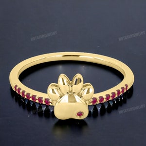 May include: Gold ring with a paw print design and a row of red gemstones around the band.
