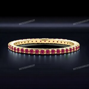 May include: A gold band ring with a row of small, red ruby stones.