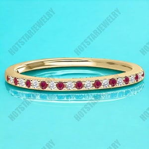 May include: A gold band ring with a row of small red and white gemstones. The ring is on a blue background.