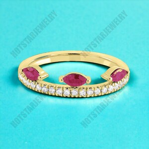 May include: A gold ring with a delicate band of small diamonds and three marquise-shaped ruby stones. The ring is open on one side, creating a unique and modern design.