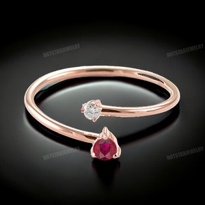 May include: A rose gold ring with a ruby and a diamond. The ring is designed with a twist, with the ruby on one side and the diamond on the other.