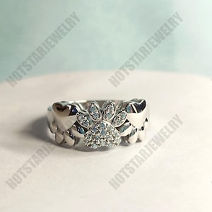 May include: A silver ring with a paw print design set with clear cubic zirconia stones. The paw print is surrounded by two heart shapes.