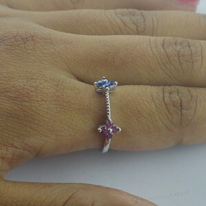 May include: A silver ring with two flower-shaped settings. The top setting has blue gemstones and the bottom setting has pink gemstones.