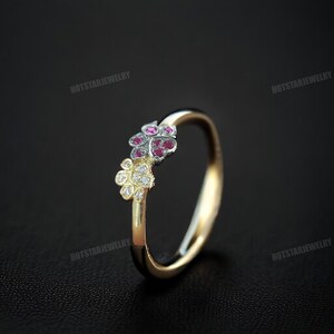 May include: A gold ring with a floral design. The ring features a cluster of small, round, red gemstones and a cluster of clear, round gemstones. The ring is set against a dark background.