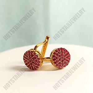 May include: A pair of gold earrings with red ruby stones. The earrings are round and have a small, delicate design.