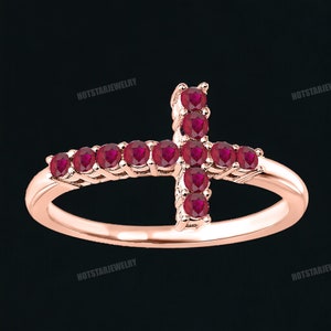 May include: A rose gold ring with a cross design set with red ruby stones.