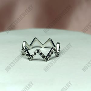 Peut inclure: Une bague en argent avec un design en zig-zag. La bague est sertie de petites pierres noires.