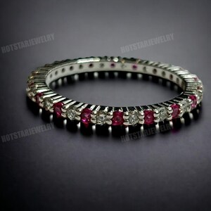 May include: A silver band ring with a row of alternating red ruby and clear round stones.