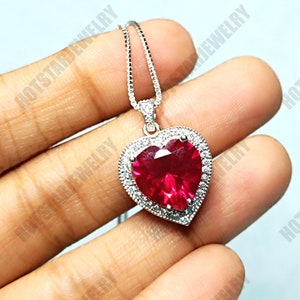 May include: A silver heart-shaped pendant necklace with a large red heart-shaped gemstone surrounded by smaller clear gemstones.