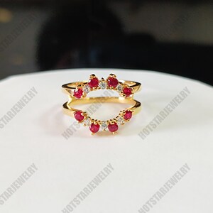 May include: Gold ring with a double band design. The top band features a row of red gemstones and smaller clear gemstones. The bottom band features a row of red gemstones.