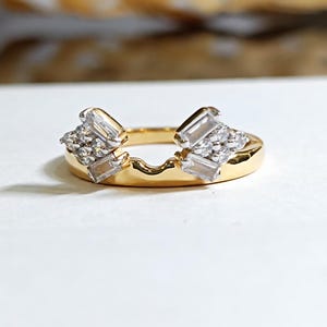 May include: A gold ring with a unique design. The ring features a curved band and two clusters of small, clear stones and larger, rectangular stones. The ring is set against a white background.