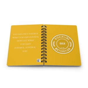 May include: Open spiral notebook with yellow pages. The left page has text in a serif font: "YOU CAN ONLY CONTROL WHAT YOU CAN CONTROL. DONT LET WHAT YOU CANT CONTROL, CONTROL YOU." The right page has a circular sticker that says "DISCIPLINE OVER MOTIVATION EST. 1982."