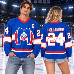 May include: A blue hockey jersey with white and red stripes, featuring a large M logo with a fleur-de-lis on the front, the letter C on the chest, and the name HOLLANDER with the number 24 in white on the back, worn by two individuals.