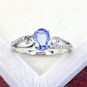 Può includere: Un anello d'argento con una pietra ovale blu e piccoli diamanti incastonati in un design delicato. L'anello è in una scatola bianca.