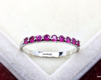 May include: A silver band ring with a row of pink gemstones. The ring is in a white box with the text "jewellerySL" on the bottom.