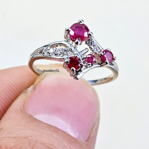 May include: A silver ring with a delicate design featuring three red ruby stones and smaller white stones.
