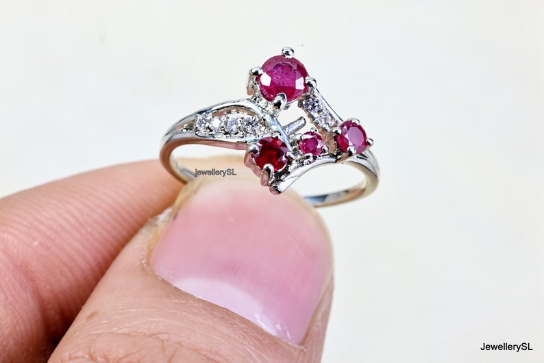 May include: A silver ring with a delicate design featuring three red ruby stones and smaller white stones.