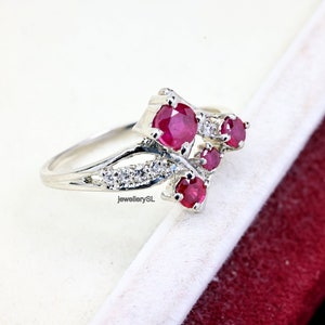 May include: A silver ring featuring a cluster of red ruby stones and smaller white diamonds. The ring has a delicate, intricate design.