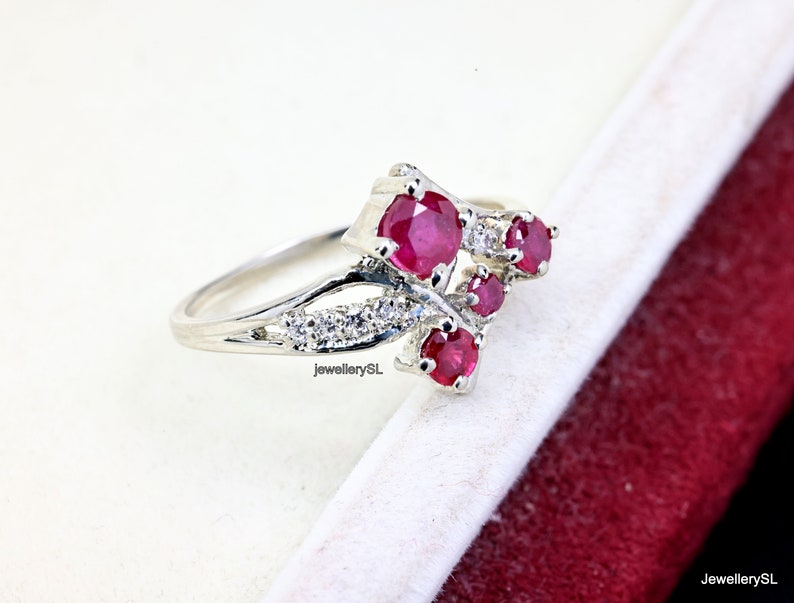 May include: A silver ring featuring a cluster of red ruby stones and smaller white diamonds. The ring has a delicate, intricate design.