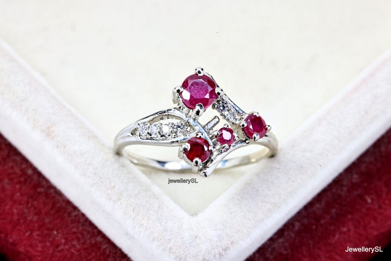 May include: A silver ring featuring a cluster of red rubies and small white diamonds. The ring has a delicate, intricate design.
