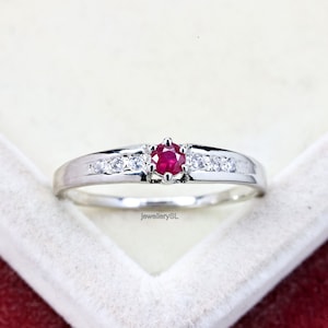 May include: A silver ring with a red ruby gemstone and small clear gemstones set in a band.