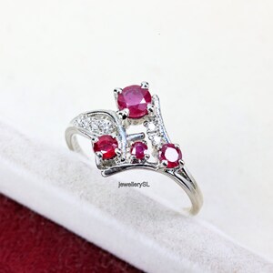 May include: A silver ring featuring a cluster of red rubies and white diamonds. The ring has a delicate, curved design.