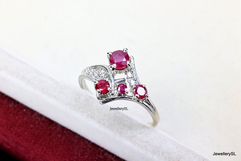 May include: A silver ring featuring a cluster of red rubies and white diamonds. The ring has a delicate, curved design.