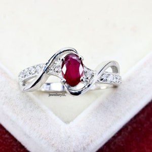 May include: A silver ring with a red oval ruby gemstone and small clear gemstones on the band.